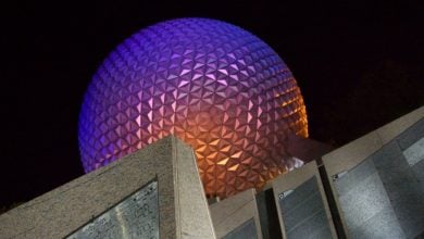 Spaceship Earth at Epcot illuminated in vibrant purple and orange hues against the night sky