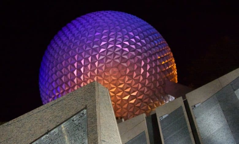 Spaceship Earth at Epcot illuminated in vibrant purple and orange hues against the night sky