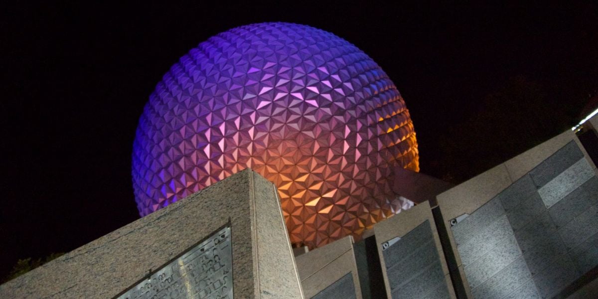 Spaceship Earth at Epcot illuminated in vibrant purple and orange hues against the night sky