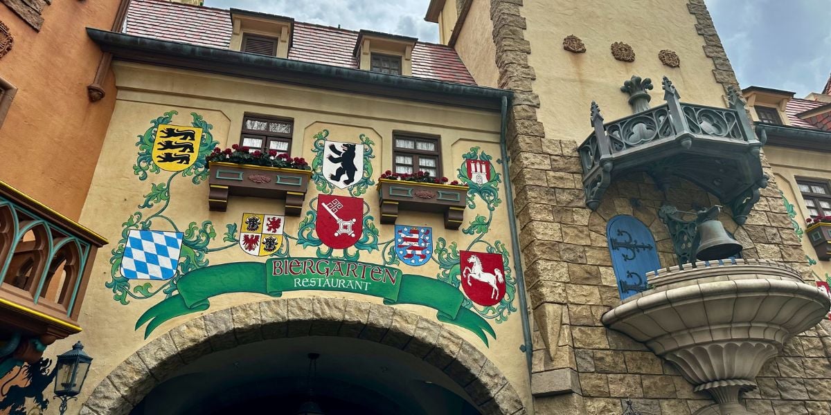 The entrance to Biergarten Restaurant at EPCOT’s Germany Pavilion, featuring vibrant German crests above the archway, invites guests into a lively Disney dining experience celebrating Bavarian culture.