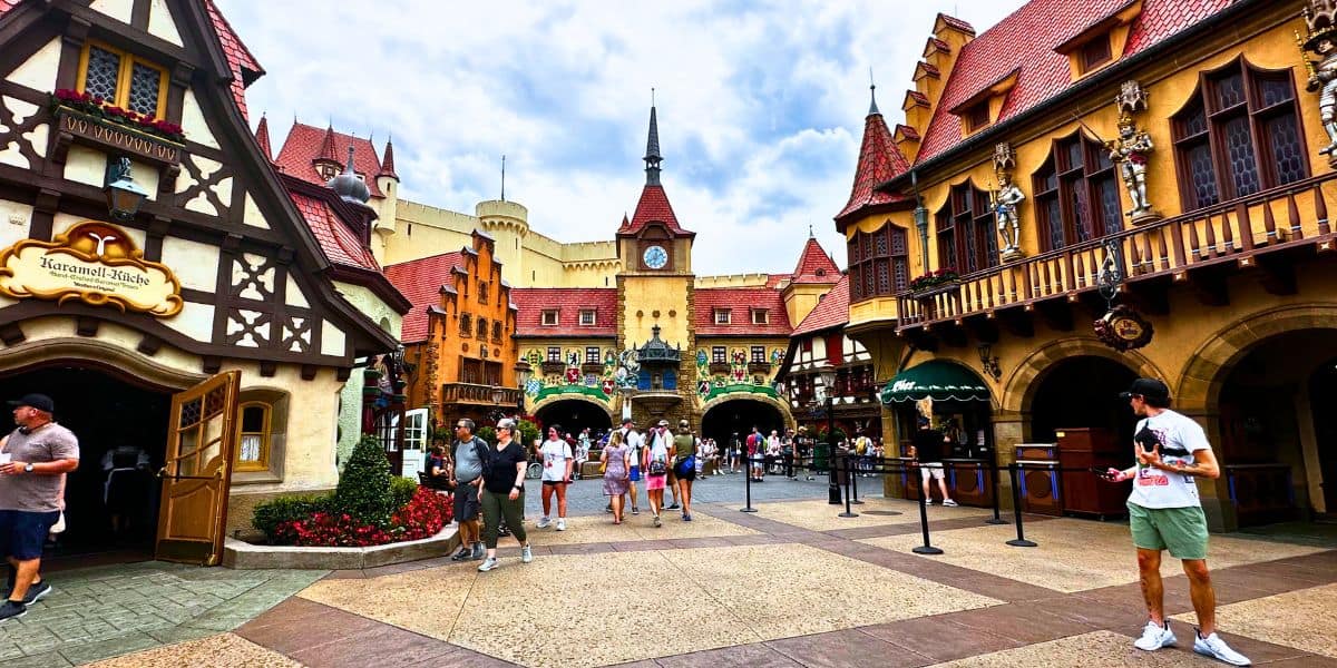 Guests explore EPCOT’s Germany Pavilion, strolling past storybook Bavarian architecture and an iconic clock tower set against a cloudy sky.