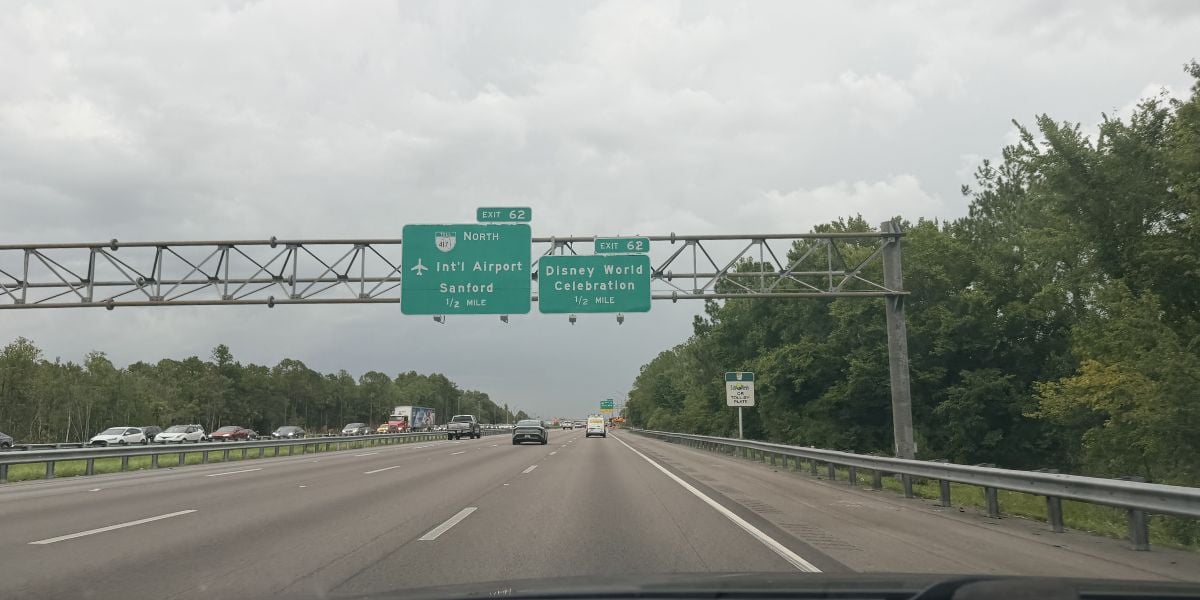 Cars driving toward green exit signs pointing to Disney World, International Airport, Sanford, and Celebration, with the Disney World sign standing out as a highlight for theme park visitors.