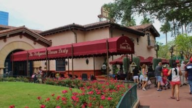 Guests gather in front of the Hollywood Brown Derby at Disney’s Hollywood Studios, under its iconic red awning with vibrant floral displays welcoming visitors.