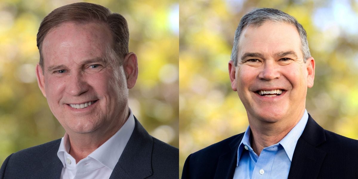 Two Disney executives in suits share a cheerful moment outside, leafy Disney World scenery blurred behind them.