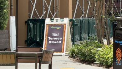 The "Tiki Terrace Closed" sign is displayed at Universal Studios near vacant patio tables, themed barriers, and a Tiki-style trash can surrounded by lush tropical plants.
