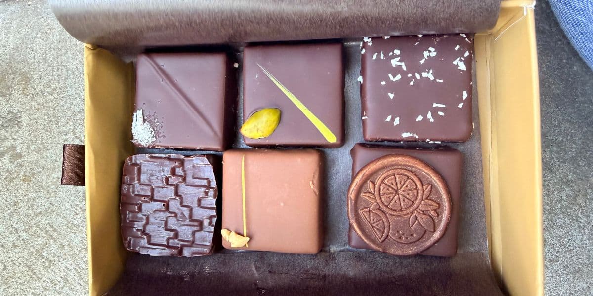 Seven gourmet chocolates in a box, each featuring unique designs, toppings, or patterns—ideal for indulging during a relaxing night at your Disney Resort after a magical day at Disney Springs, or as the perfect sweet treat to celebrate your Disney World Halloween park ticket.
