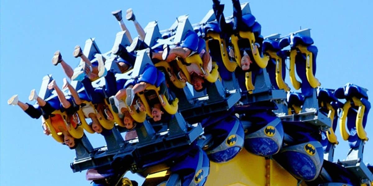 Thrill-seekers soar upside down on BATMAN: The Ride beneath a bright blue sky at Six Flags.