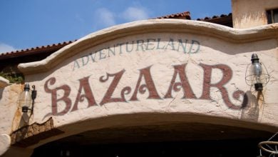 Adventureland Bazaar sign welcomes guests beneath a classic beige stucco archway, framed by themed lanterns and bright blue Disneyland skies.