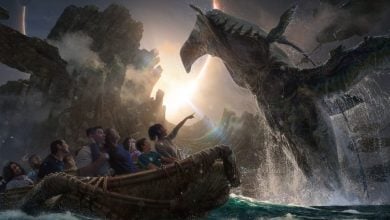 Guests aboard a themed adventure ride thrill as a massive, dragon-like creature rises dramatically from the water, bringing the fantasy world to life.