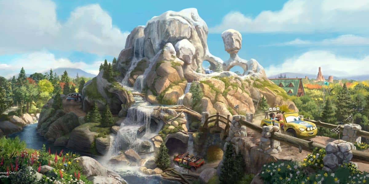Radiator Springs Racers zoom along the track, winding past majestic rocky mountains with cascading waterfalls, lush trees, and a bright blue sky inside Cars Land at Disney California Adventure.