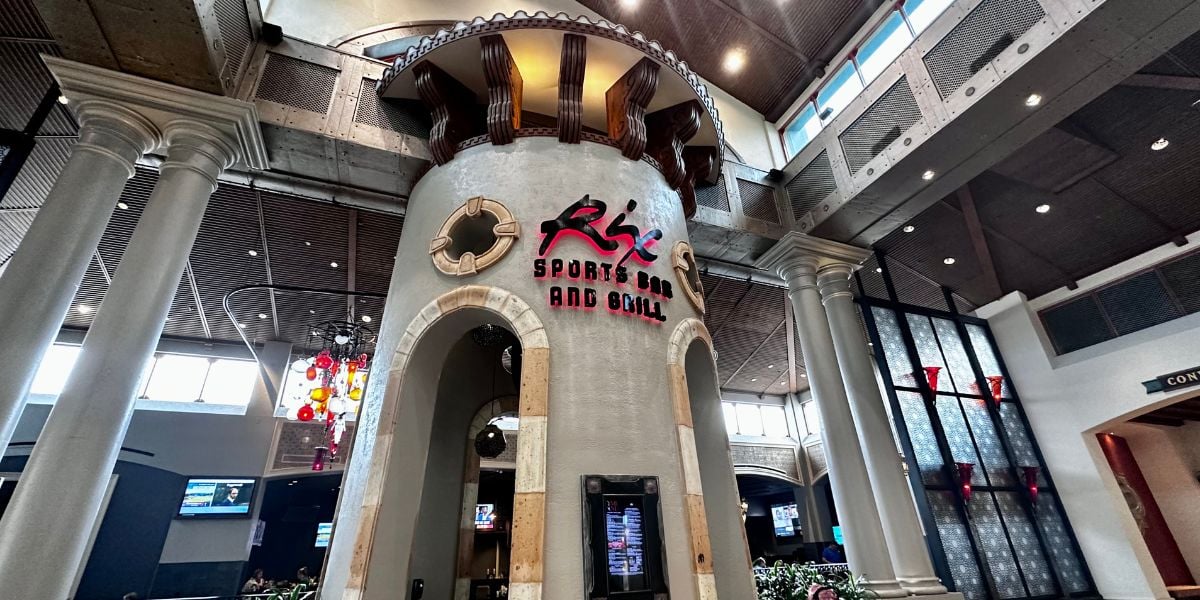 A round stone tower rises within the lively interior, topped with a vibrant sign for “Rix Sports Bar and Grill” in playful pink and red lettering, blending right into the immersive Disney World atmosphere—perfect for fans seeking themed dining and entertainment.