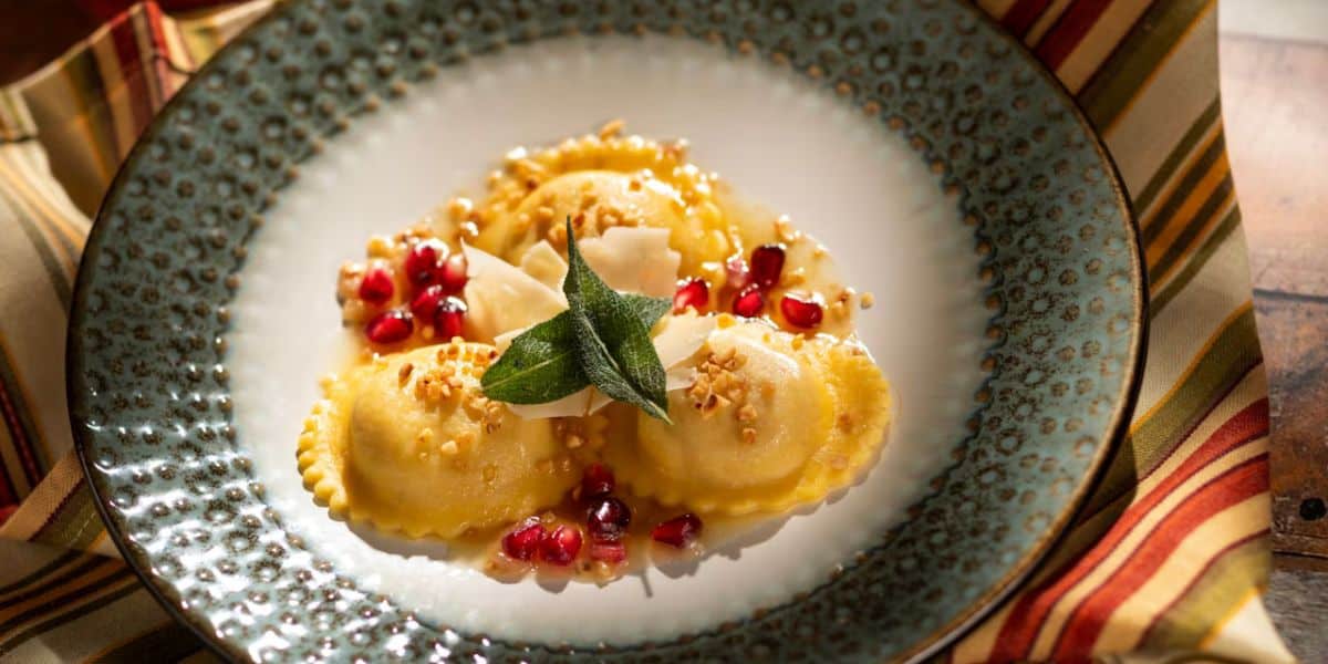 Ravioli served EPCOT-style with vibrant pomegranate seeds, shaved cheese, crunchy nuts, and fresh sage on a decorative plate—a must-try bite for any Disney World Food & Wine Festival fan.