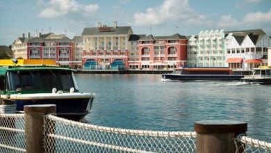 Vibrant Disney resort buildings and charming boats line the scenic waterfront, with a rope fence in the foreground and clear blue skies overhead—a lively, immersive atmosphere perfect for theme park fans soaking up exclusive Disney resort benefits.