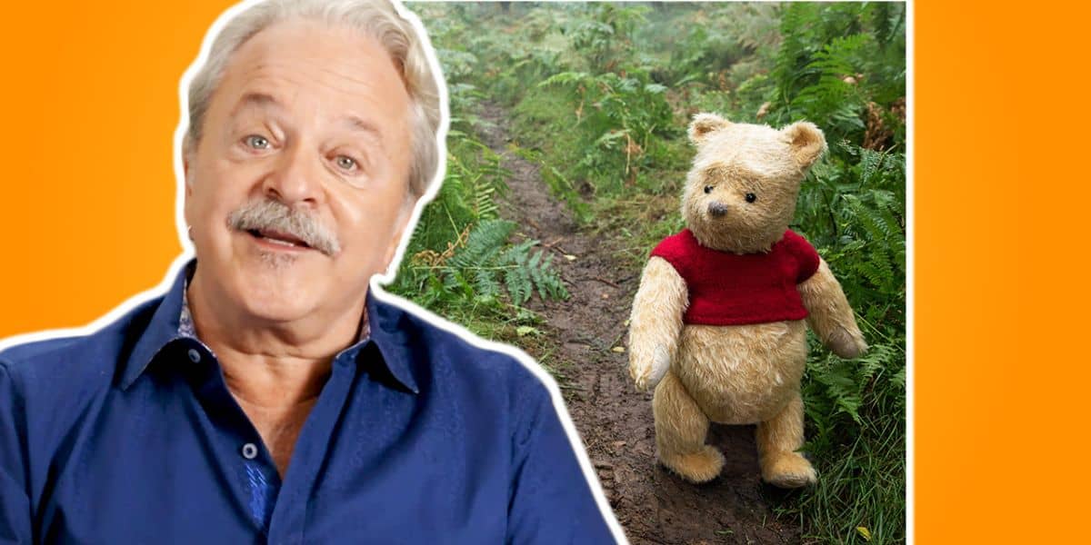 Jim Cummings, the Disney Legend, smiles alongside Winnie the Pooh in his iconic red shirt as they stroll down a woodland path, capturing the enchanting spirit of beloved character meet-and-greets found at Disney parks.