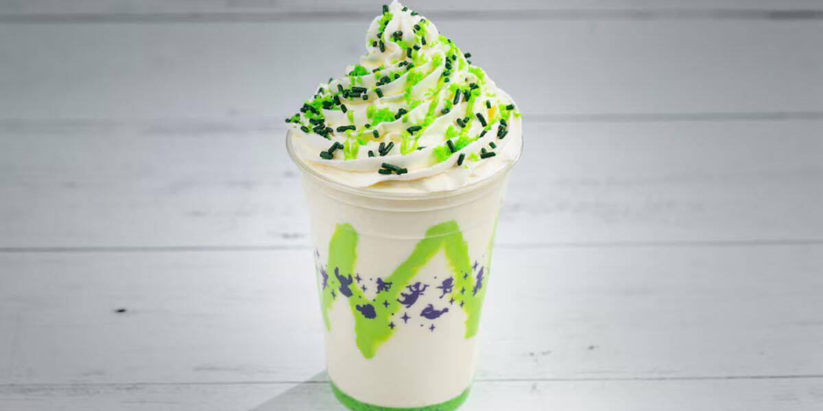 A vanilla milkshake from the park’s snack stand, served in a clear plastic cup and topped with festive green and black sprinkles plus a swirl of whipped cream—perfect for sipping while exploring attractions.