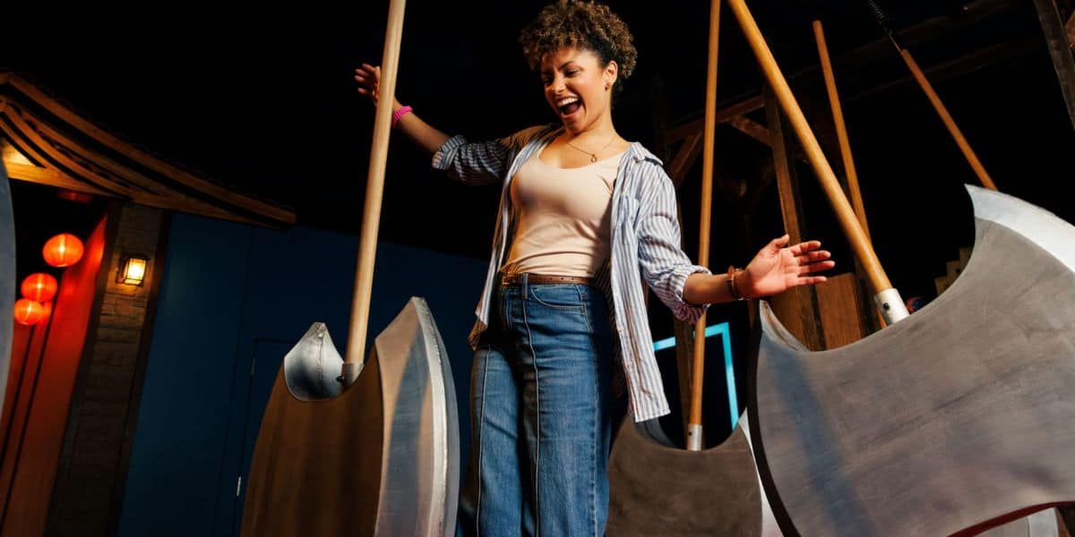 A guest navigates the thrilling swinging axe challenge inside Disney Springs’ latest indoor adventure attraction, immersed in an adrenaline-pumping escape room experience.