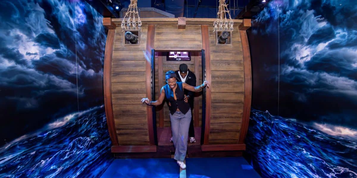 Guests step off a life-sized wooden ship into a vividly immersive set featuring stormy seas and dramatic lightning effects painted across the walls, as part of Disney Springs’ new cutting-edge adventure attraction redefining interactive experiences.