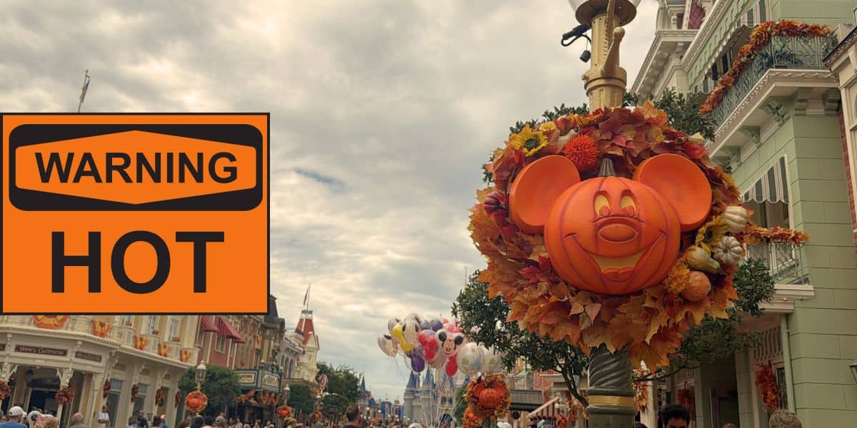 A festive Mickey pumpkin wreath decorates a Main Street lamp post at Disney World, surrounded by autumn leaves and set against cloudy skies, with a nearby “WARNING HOT” sign adding to the lively park atmosphere.