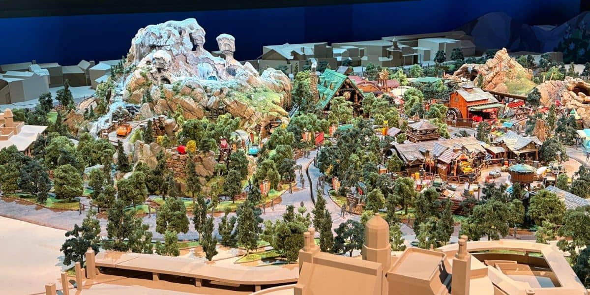 Detailed scale model of a theme park land featuring lush landscaping, themed buildings, and dramatic rocky mountain backdrops, highlighting immersive attractions and vibrant park design.