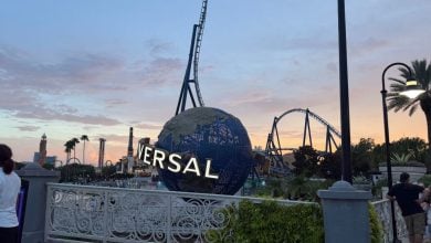 Universal Studios globe and thrilling roller coaster glowing at sunset, with excited guests and iconic palm trees creating the perfect theme park atmosphere.