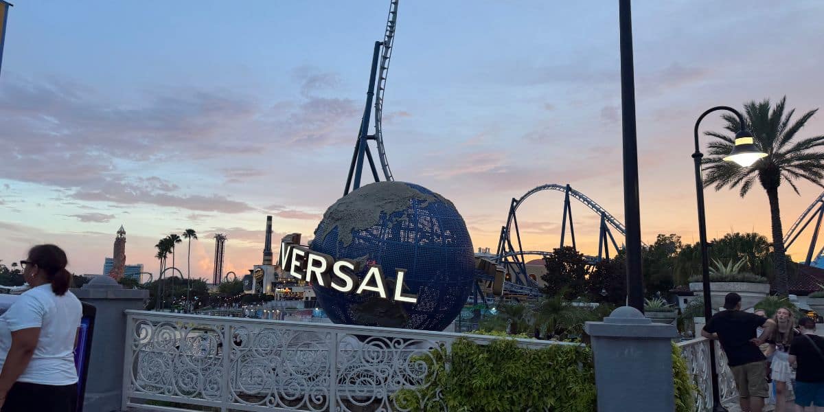 Universal Studios globe and thrilling roller coaster glowing at sunset, with excited guests and iconic palm trees creating the perfect theme park atmosphere.