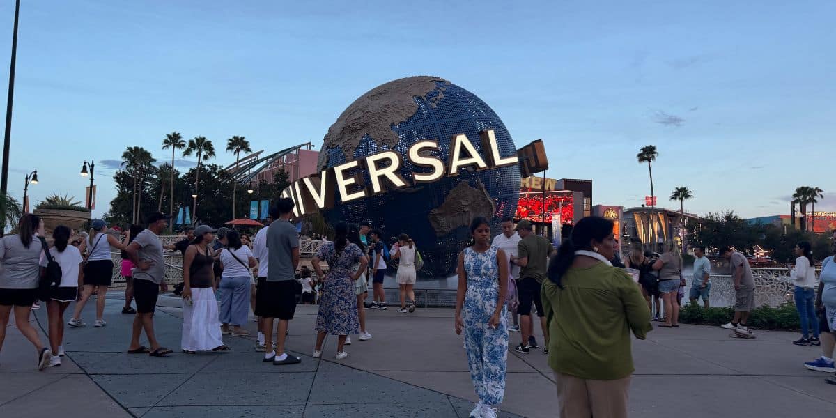 Visitors pose and take photos in front of the iconic Universal Studios globe at the park entrance plaza, enjoying a bright, sunny day.