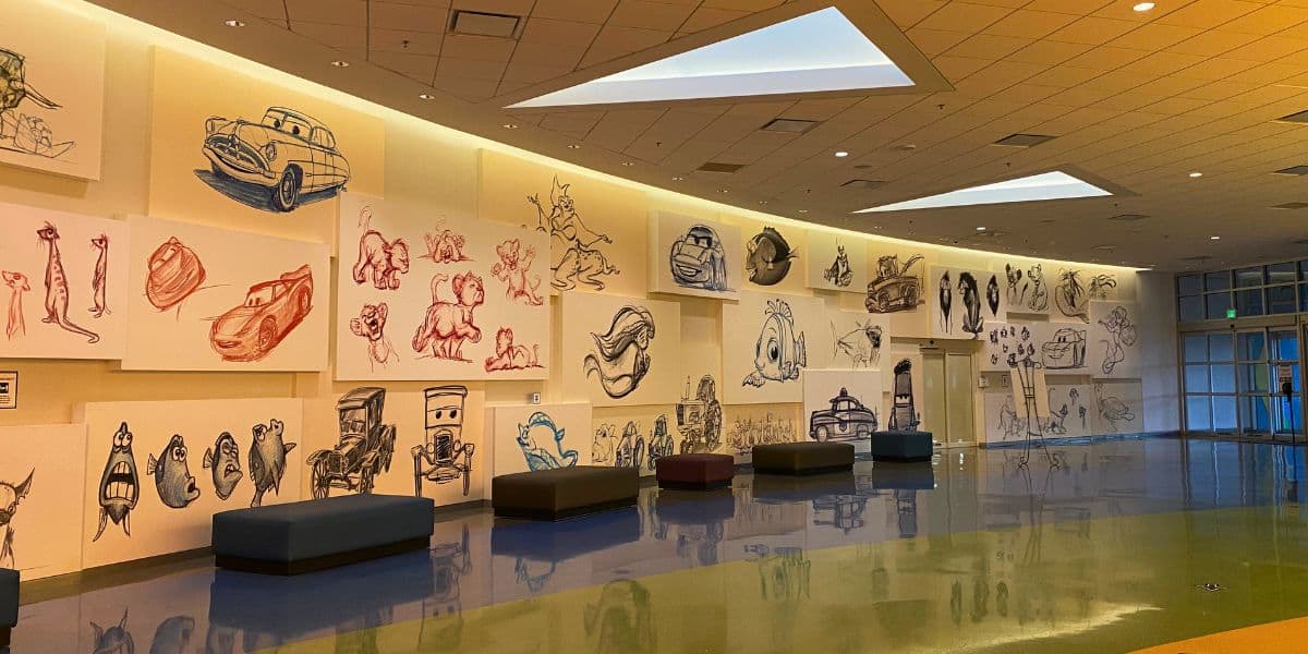 Wall adorned with lively sketches of beloved Disney characters, iconic cars, and whimsical animals at the Art of Animation Resort in Disney World; shiny floors reflect inviting benches below the colorful artwork. Immerse yourself in this imaginative gallery when you visit in 2027.
