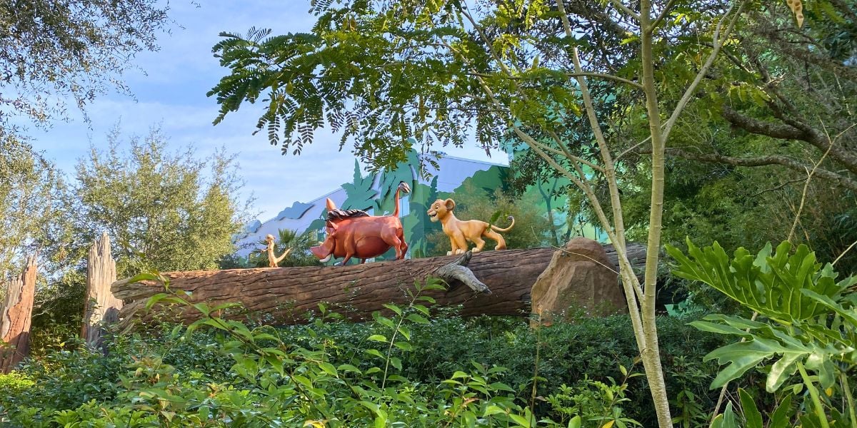 Simba, Timon, and Pumbaa statues strike a playful pose atop a log surrounded by vibrant jungle foliage at Disney World’s Art of Animation Resort, creating a lively Lion King display that transports guests straight into the magic for their 2027 adventure.