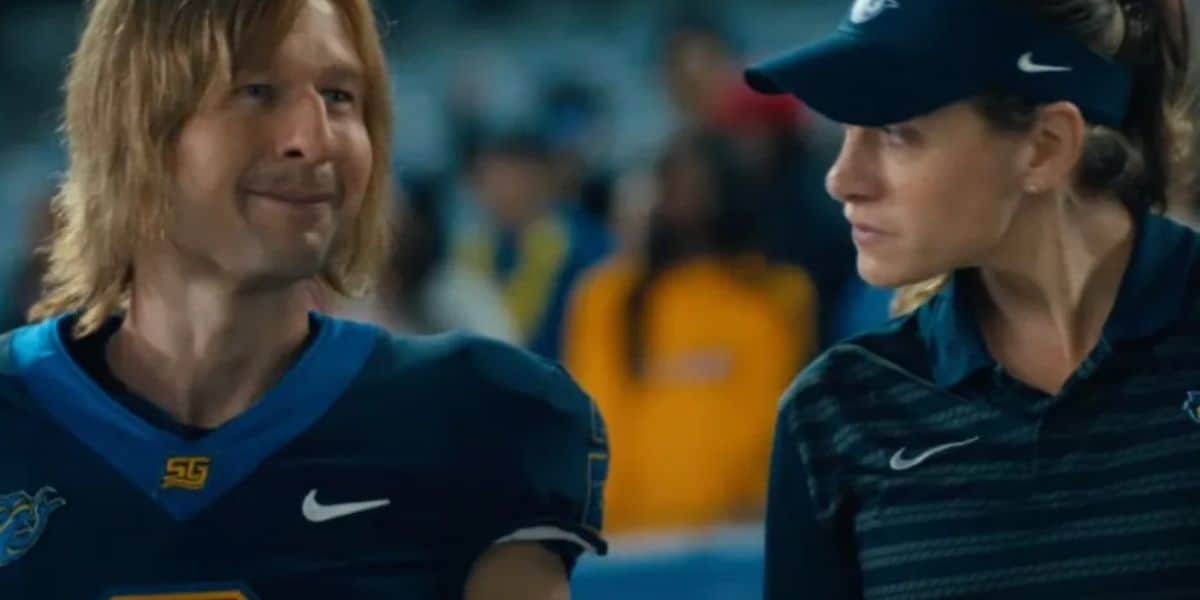 Chad Powers, suited up in his football gear, chats with a woman sporting a visor and striped jacket on the stadium field, bringing a lively sports scene to life for fans.