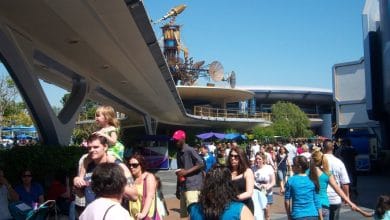 Guests stroll beneath sleek, cutting-edge architecture at EPCOT on a bright, sunny day.