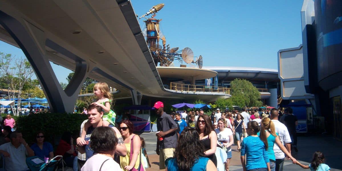 Guests stroll beneath sleek, cutting-edge architecture at EPCOT on a bright, sunny day.