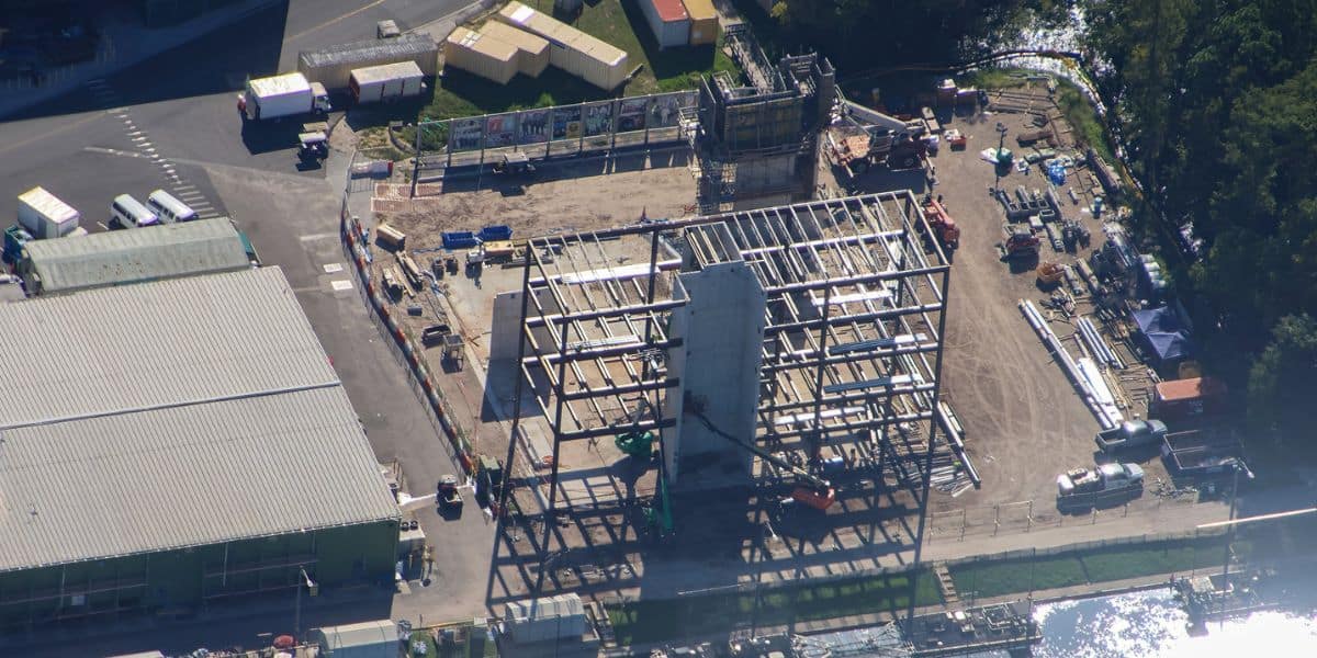 Bird’s-eye view of the steel framework for a new attraction rising in a lively theme park construction zone, with colorful building materials adding to the excitement of future rides and entertainment spaces.