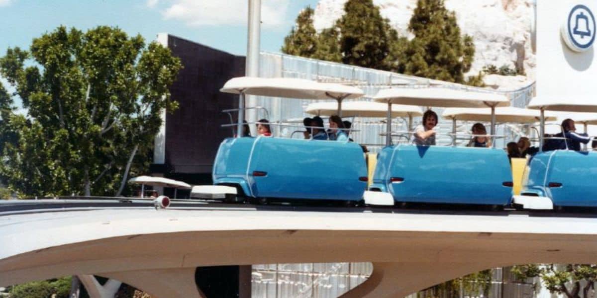 Guests enjoy a scenic ride aboard the iconic blue Monorail gliding along elevated tracks, surrounded by lush greenery and bathed in sunshine.