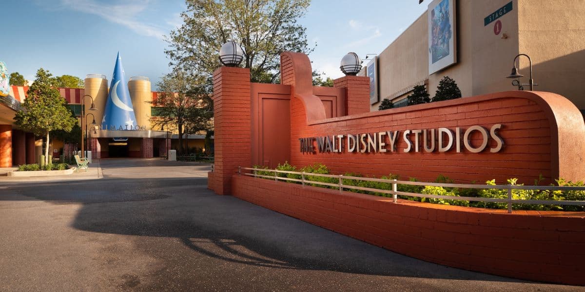 Main entrance to The Walt Disney Studios, featuring iconic orange walls, lush landscaping, and the recognizable blue Sorcerer’s Hat welcoming visitors.