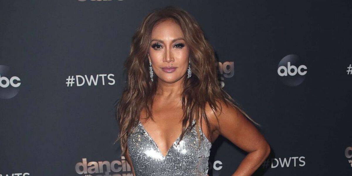 A “Dancing With The Stars” celebrity dazzles in a sparkling silver sequin dress on the show’s signature red carpet, surrounded by iconic logos, making an appearance just after the thrilling surprises of Week One Eliminations—a must-see moment for entertainment fans.
