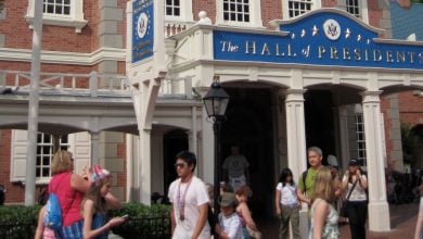 Guests stroll past the Hall of Presidents entrance at Magic Kingdom on a bright, sunny day.