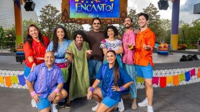 Encanto performers in vibrant costumes strike a festive pose on stage beneath the colorful Encanto sign, bringing lively Disney World entertainment to life.