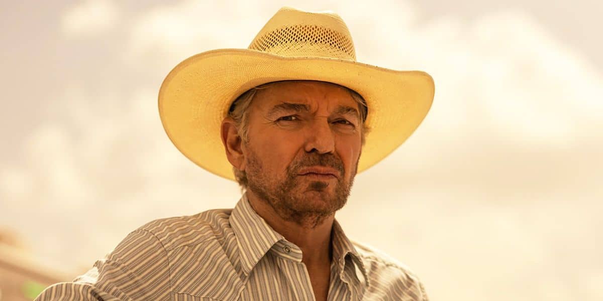 Billy Bob, dressed in a straw cowboy hat and a striped shirt, poses outdoors beneath a dramatic, cloud-filled sky—capturing the rugged spirit featured in Paramount’s Landman series.
