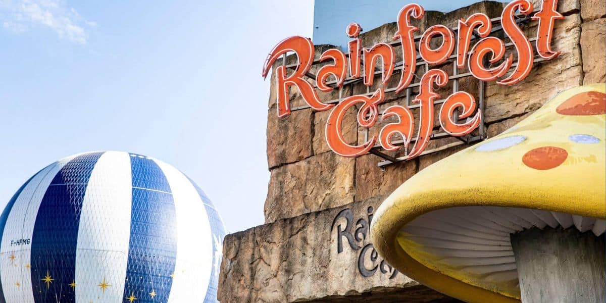 Rainforest Cafe sign with its signature giant mushroom, set against a blue-striped hot air balloon in Disney Village at Disneyland Paris, captured before the beloved restaurant’s permanent closure.