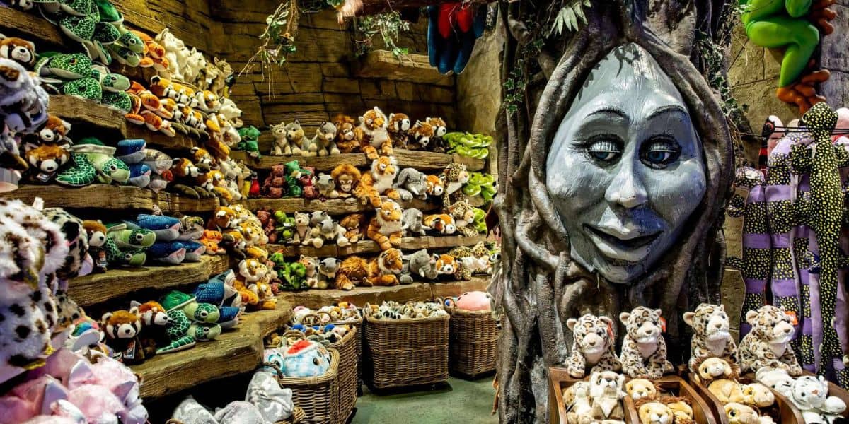 Plush toys arranged on shelves and in baskets surround an enchanting tree with a giant, whimsical face carved into its trunk, capturing the playful atmosphere of Disney Village at Disneyland Paris.