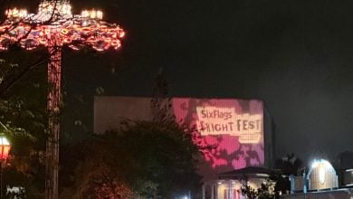 A Six Flags Fright Fest billboard at night, pictured next to a spinning, lit-up ride.