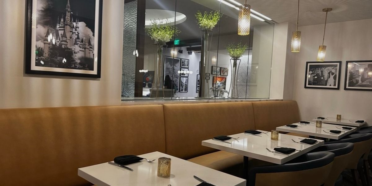 Chic restaurant with tan booth seating, crisp white tables, black napkins, and Disney-inspired framed art on the walls—inviting guests to relax in a space that channels the iconic mid-century modern vibe of Disney’s Contemporary Resort.