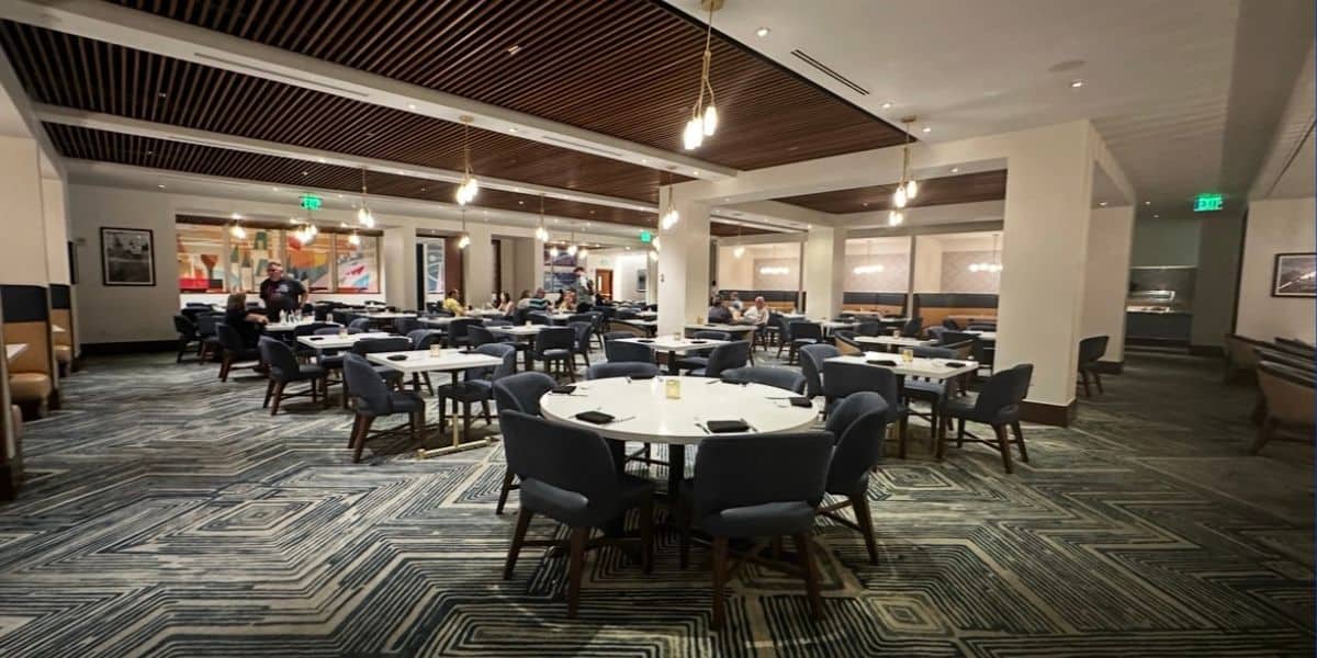 Vibrant dining area at Disney’s Contemporary Resort featuring round tables, blue chairs, and stylish modern lighting; Disney park guests are seated throughout the space, savoring iconic Disney cuisine in a fun, energetic atmosphere.