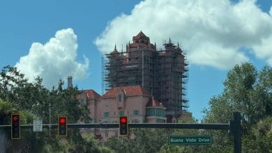 The iconic pink facade of a Disneyland building under renovation, surrounded by trees and visible from the street, with the Buena Vista Drive sign in view.