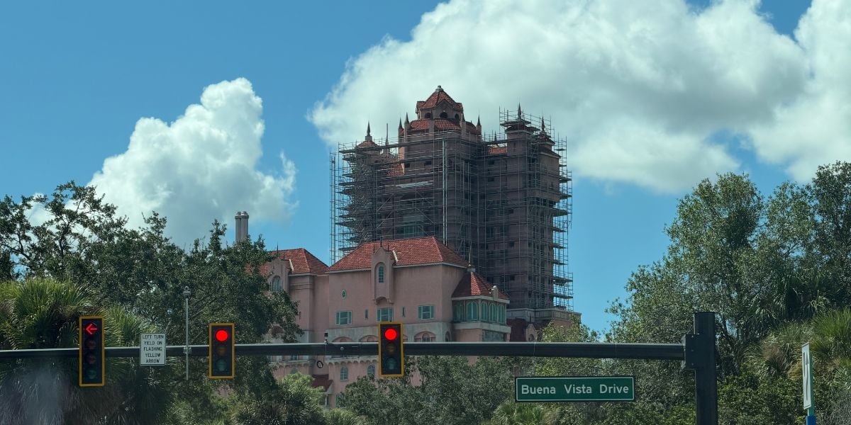 The iconic pink facade of a Disneyland building under renovation, surrounded by trees and visible from the street, with the Buena Vista Drive sign in view.