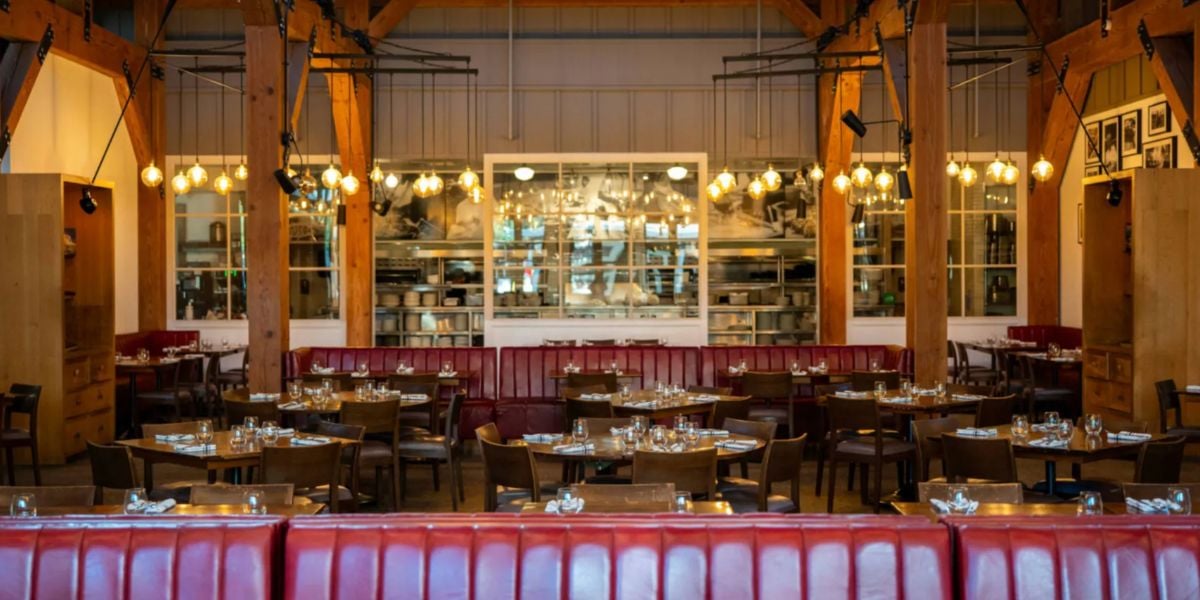 The former Wolfgang Puck Bar & Grill at Disney Springs, featuring vibrant red booths, wooden tables, stylish hanging lights, and a view of the open kitchen where world-class dishes were once prepared, now sits closed—a nostalgic spot for Disney fans and foodies alike.