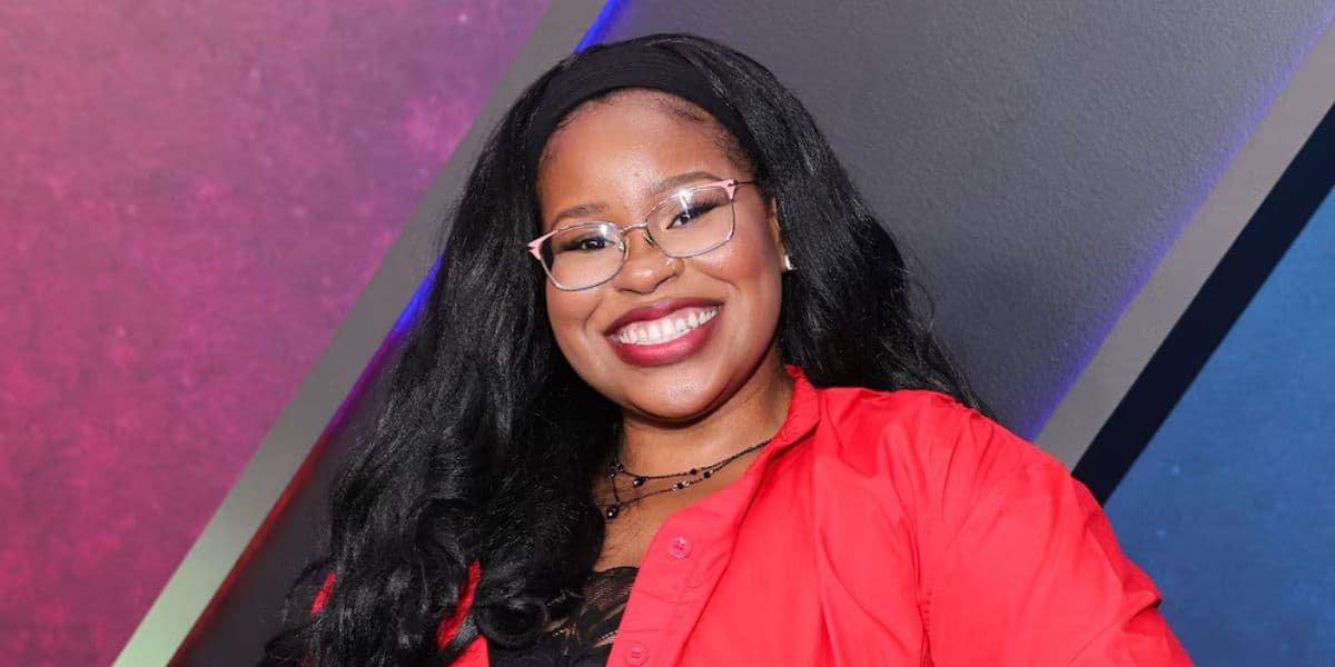 A smiling guest with long black hair, glasses, and a red shirt poses in front of a backdrop inspired by the bold, energetic designs often seen on Disney Channel shows, capturing the playful spirit of Disney entertainment venues.