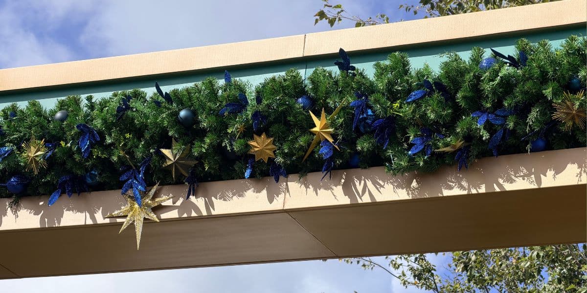Evergreen garland with blue ornaments and gold stars adorning a holiday archway at the theme park entrance.