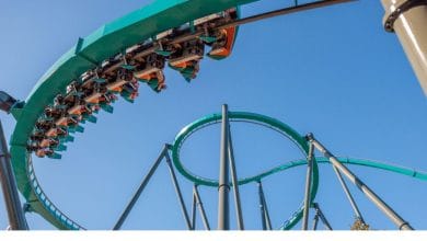 Inverted roller coaster train navigating a teal track loop at a theme park against a clear blue sky.