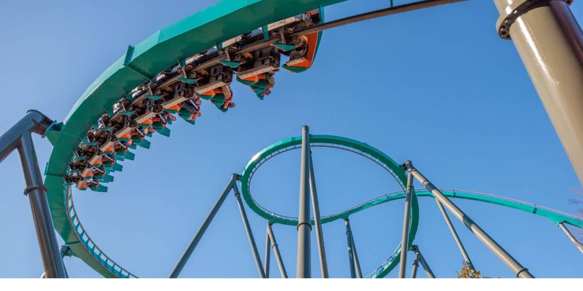 Inverted roller coaster train navigating a teal track loop at a theme park against a clear blue sky.